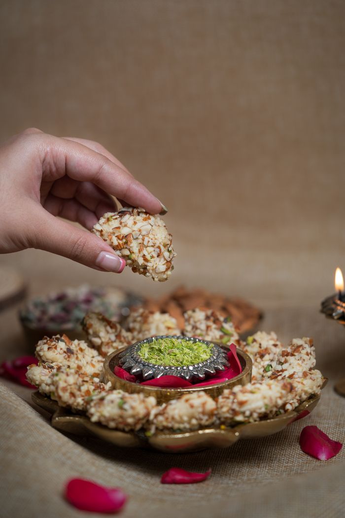 A close-up of Indian sweets arranged for a cultural celebration, highlighting a woman's hand picking sweets.